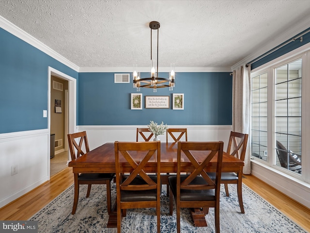 dining space with a textured ceiling, an inviting chandelier, light hardwood / wood-style flooring, and ornamental molding