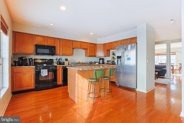 kitchen with a kitchen bar, decorative columns, a center island, light hardwood / wood-style floors, and black appliances