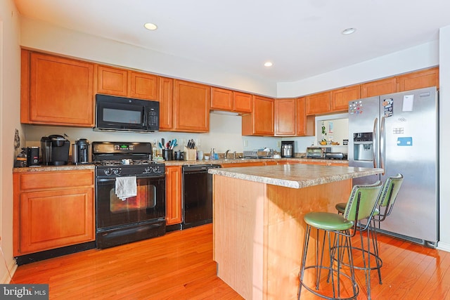 kitchen with sink, a center island, light hardwood / wood-style flooring, a kitchen breakfast bar, and black appliances