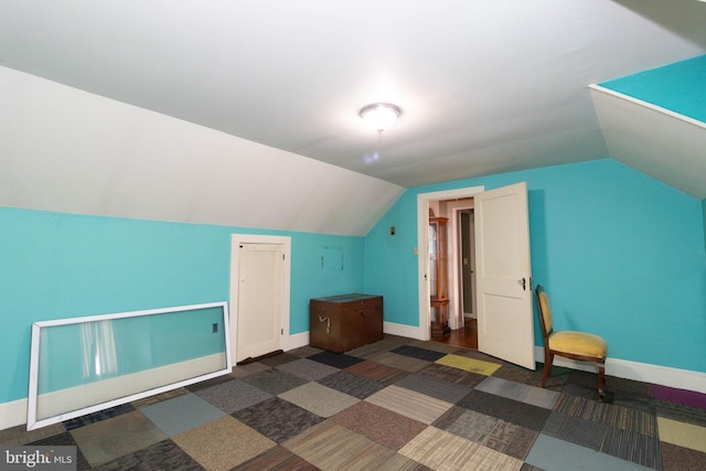 additional living space featuring lofted ceiling and dark colored carpet