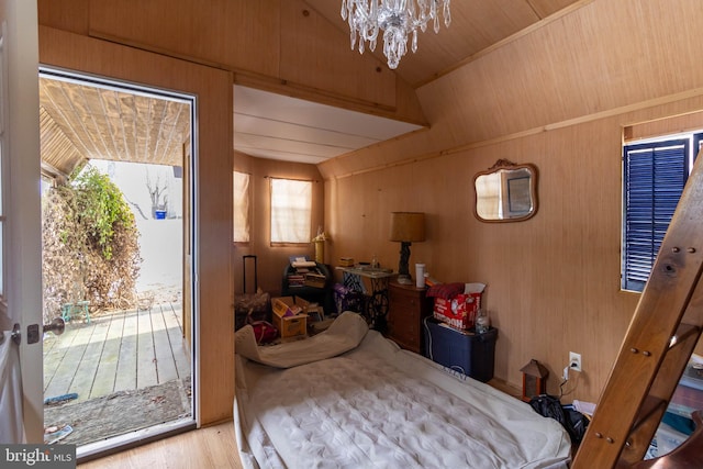 bedroom featuring wooden walls, access to exterior, light hardwood / wood-style floors, and a notable chandelier