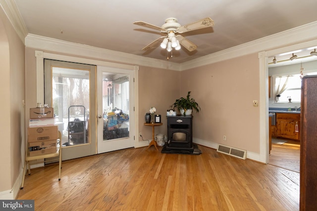 sitting room featuring ornamental molding, a wood stove, ceiling fan, and light wood-type flooring