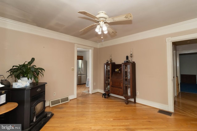 interior space with ceiling fan, ornamental molding, light hardwood / wood-style floors, and a wood stove