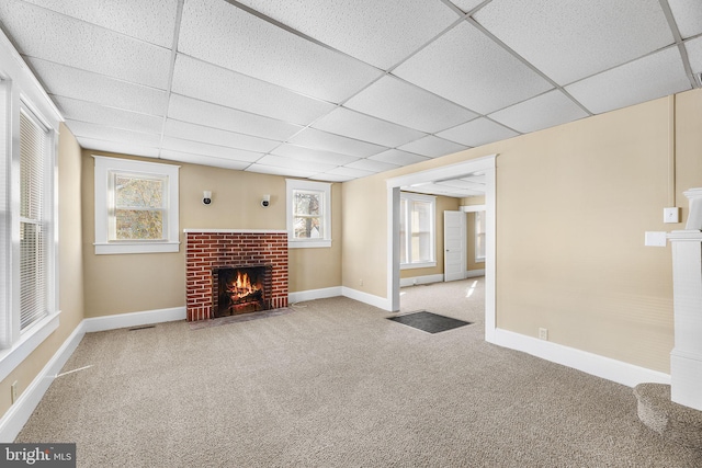 unfurnished living room with carpet, a brick fireplace, and a drop ceiling