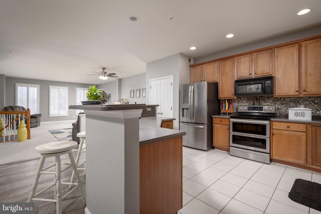 kitchen featuring a center island, appliances with stainless steel finishes, a kitchen breakfast bar, ceiling fan, and backsplash