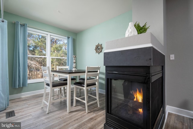 dining room with wood-type flooring and a multi sided fireplace