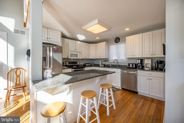 kitchen with sink, appliances with stainless steel finishes, white cabinetry, a kitchen bar, and light wood-type flooring