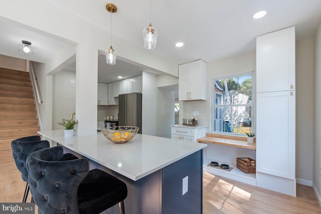 kitchen featuring stainless steel refrigerator, light hardwood / wood-style floors, white cabinets, a kitchen bar, and decorative light fixtures