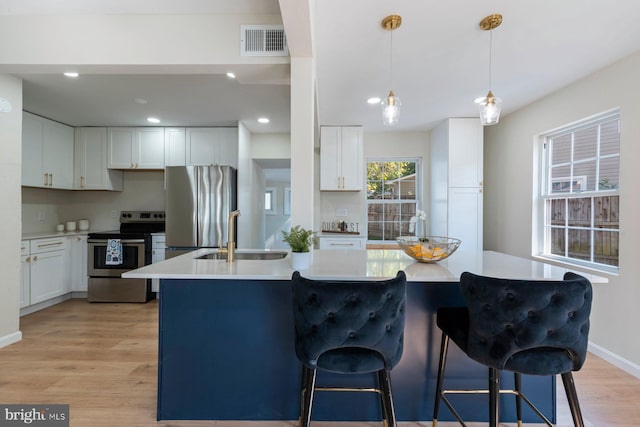 kitchen with sink, hanging light fixtures, light wood-type flooring, appliances with stainless steel finishes, and white cabinets