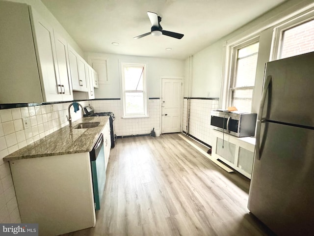 kitchen featuring stainless steel appliances, a sink, white cabinetry, dark stone counters, and a wainscoted wall