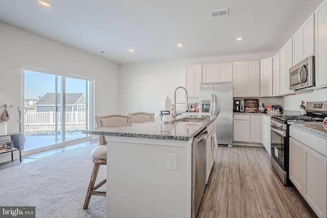 kitchen with sink, white cabinetry, an island with sink, a breakfast bar area, and stainless steel appliances