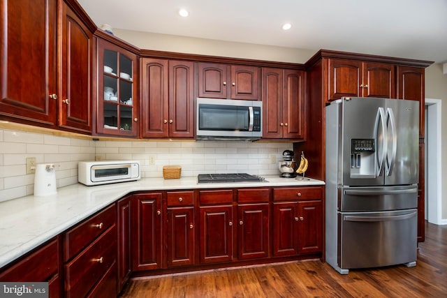 kitchen with tasteful backsplash, stainless steel appliances, dark hardwood / wood-style floors, and light stone counters