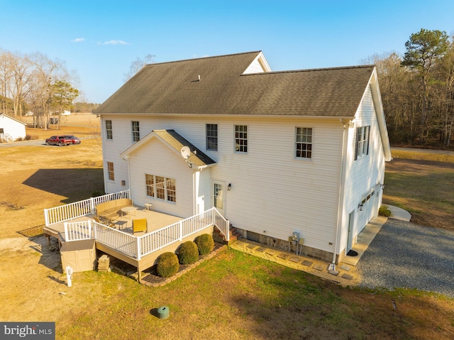 rear view of house featuring a wooden deck, a garage, and a lawn