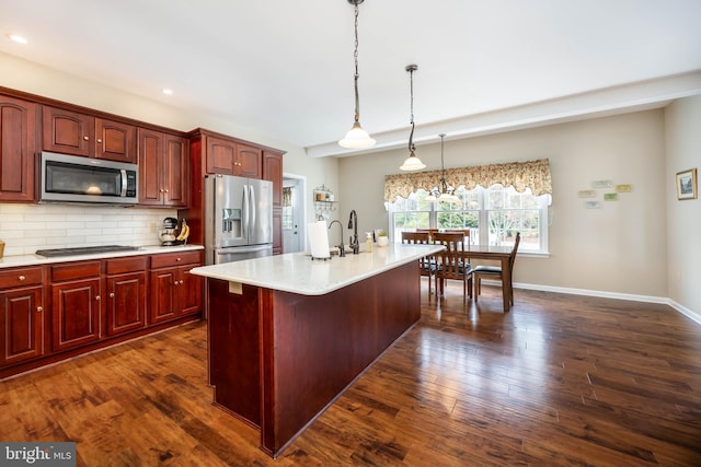 kitchen with a kitchen island with sink, hanging light fixtures, stainless steel appliances, tasteful backsplash, and dark hardwood / wood-style flooring