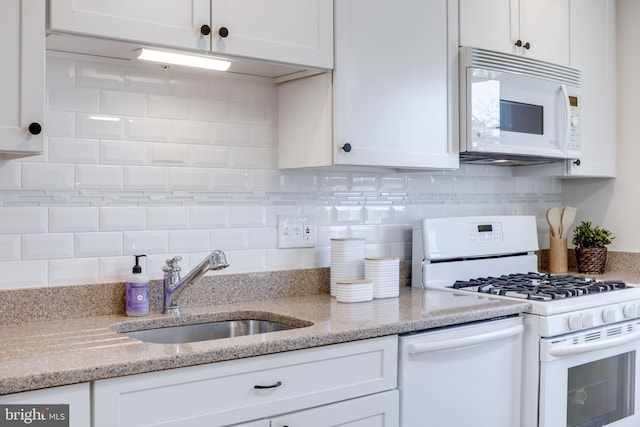 kitchen with a sink, white appliances, and white cabinetry