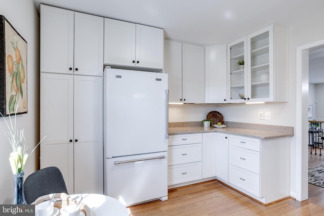 kitchen featuring glass insert cabinets, light wood-type flooring, light countertops, and freestanding refrigerator