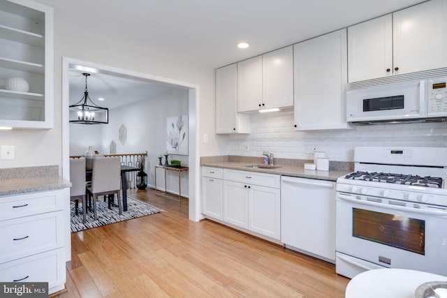 kitchen featuring light wood finished floors, tasteful backsplash, white cabinets, white appliances, and a sink