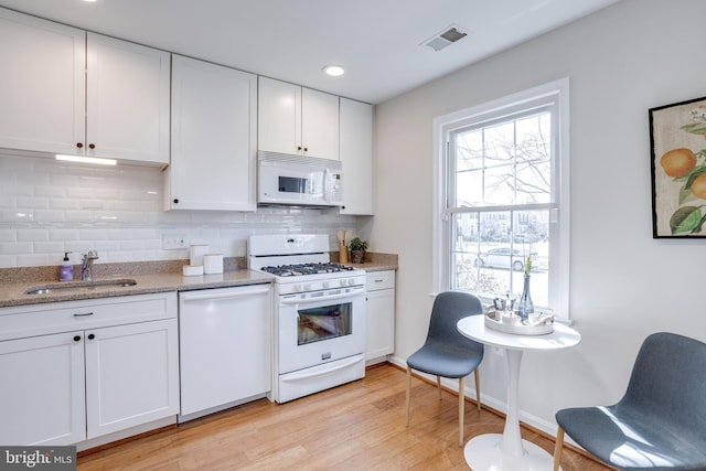 kitchen with white appliances, a sink, white cabinets, light wood-type flooring, and backsplash