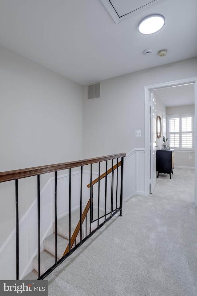 hall featuring visible vents, carpet, an upstairs landing, wainscoting, and a decorative wall