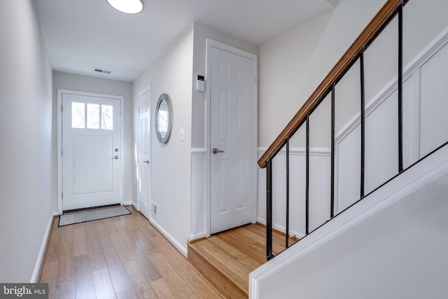 foyer entrance with visible vents, light wood-type flooring, stairs, and baseboards