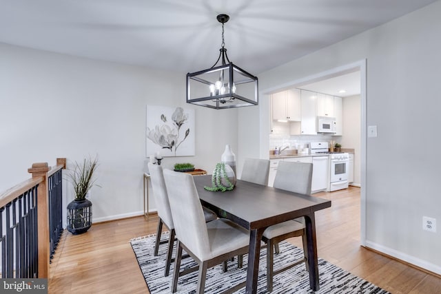 dining space with a chandelier, baseboards, and light wood-style flooring