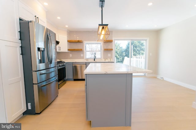 kitchen with decorative light fixtures, white cabinets, a center island, stainless steel appliances, and light stone countertops