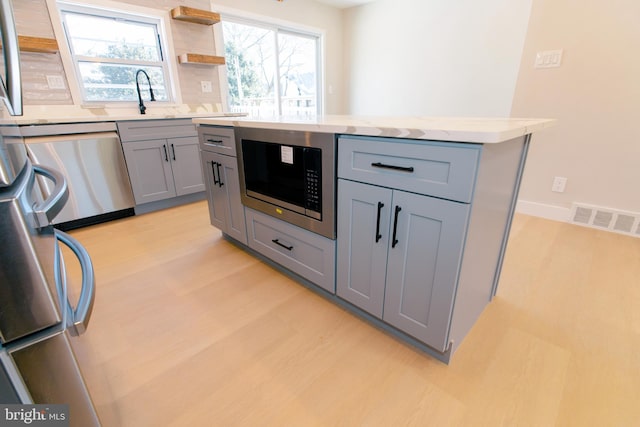 kitchen with sink, appliances with stainless steel finishes, gray cabinetry, a center island, and light hardwood / wood-style floors