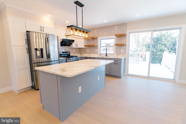 kitchen featuring a center island, appliances with stainless steel finishes, pendant lighting, range hood, and white cabinets