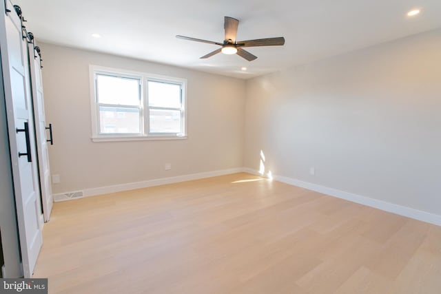 unfurnished room featuring ceiling fan, a barn door, and light hardwood / wood-style flooring