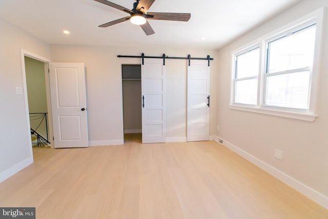 unfurnished bedroom featuring ceiling fan, a barn door, light wood-type flooring, and a closet