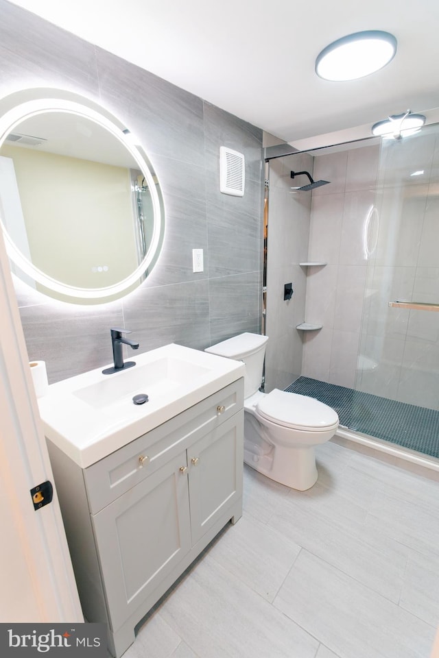 bathroom with vanity, toilet, a shower with door, and tile walls