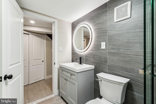 bathroom with hardwood / wood-style flooring, vanity, tile walls, and toilet