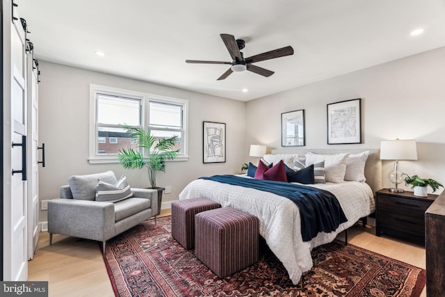 bedroom with ceiling fan, a barn door, and light hardwood / wood-style flooring