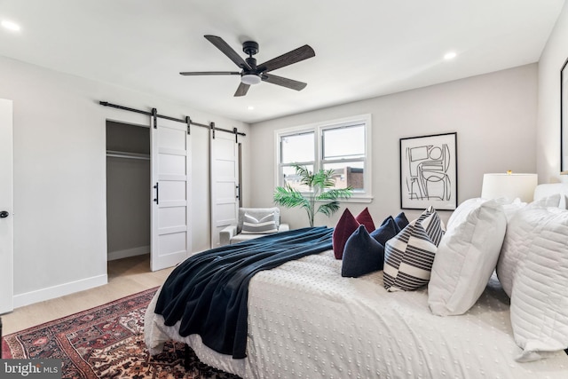 bedroom with a barn door, ceiling fan, and light hardwood / wood-style flooring