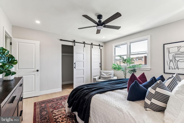 bedroom with ceiling fan, a barn door, and light wood-type flooring