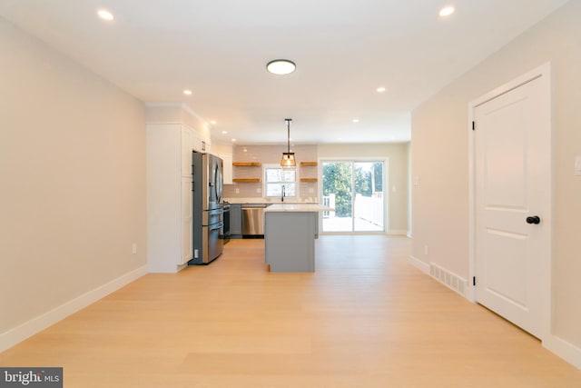 kitchen with a kitchen island, stainless steel appliances, decorative light fixtures, and light hardwood / wood-style flooring