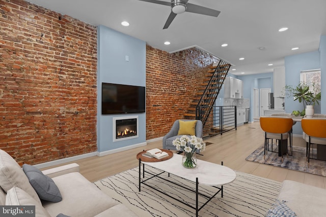 living room with light hardwood / wood-style floors, brick wall, and ceiling fan