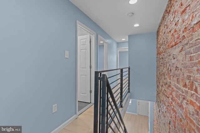 hall with light hardwood / wood-style floors and brick wall