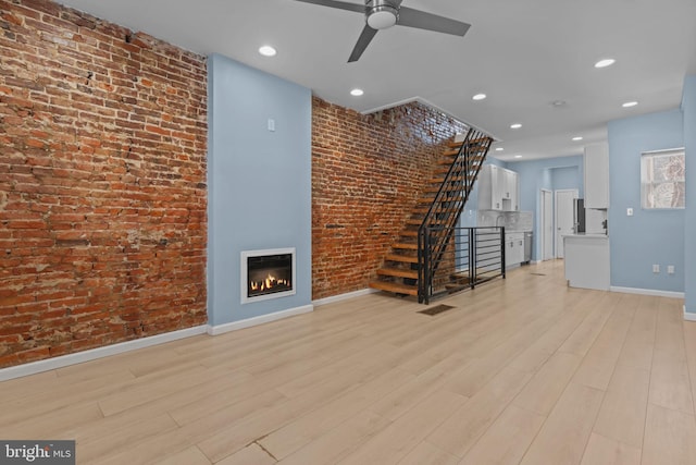 unfurnished living room featuring ceiling fan, brick wall, and light hardwood / wood-style flooring