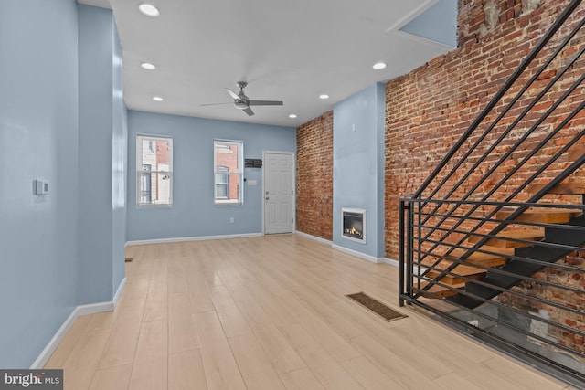 foyer with ceiling fan, brick wall, and light wood-type flooring