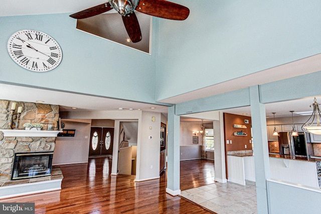 living room featuring baseboards, ceiling fan, a stone fireplace, a towering ceiling, and wood finished floors