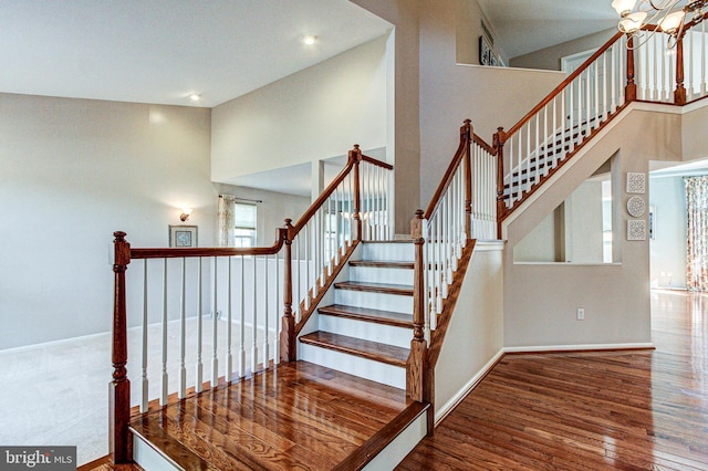 staircase featuring a notable chandelier, wood finished floors, baseboards, and a towering ceiling