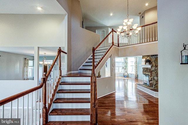 stairway with a high ceiling, a notable chandelier, a stone fireplace, and wood finished floors