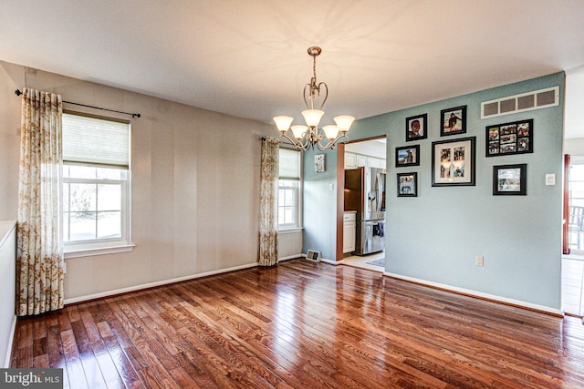 spare room with baseboards, visible vents, wood-type flooring, and an inviting chandelier