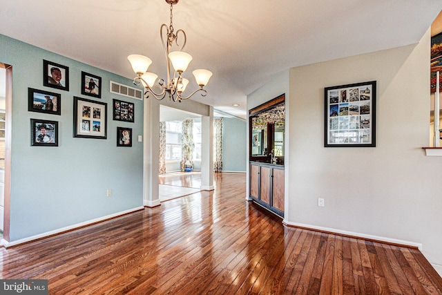 unfurnished dining area featuring hardwood / wood-style floors, a notable chandelier, visible vents, and baseboards