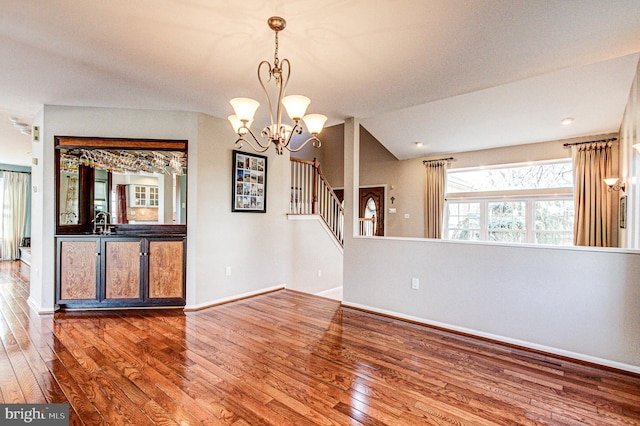 unfurnished room featuring baseboards, a chandelier, stairway, vaulted ceiling, and wood-type flooring