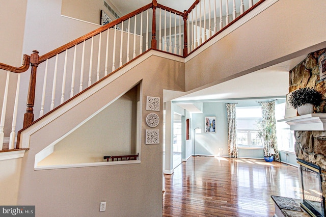 foyer entrance with wood finished floors, baseboards, a high ceiling, a stone fireplace, and stairs