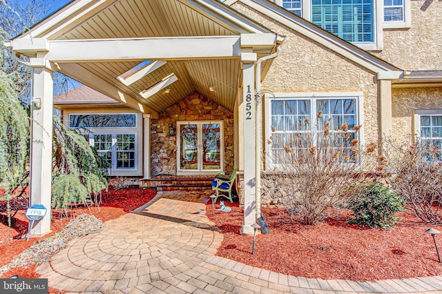 property entrance featuring stucco siding, stone siding, and french doors