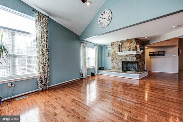 unfurnished living room with wood finished floors, visible vents, baseboards, a stone fireplace, and vaulted ceiling