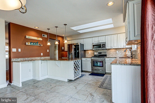 kitchen with a sink, stainless steel appliances, a peninsula, a skylight, and stone counters